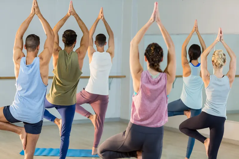 Cours collectif de yoga : élèves en posture de l’arbre, mains jointes au-dessus de la tête